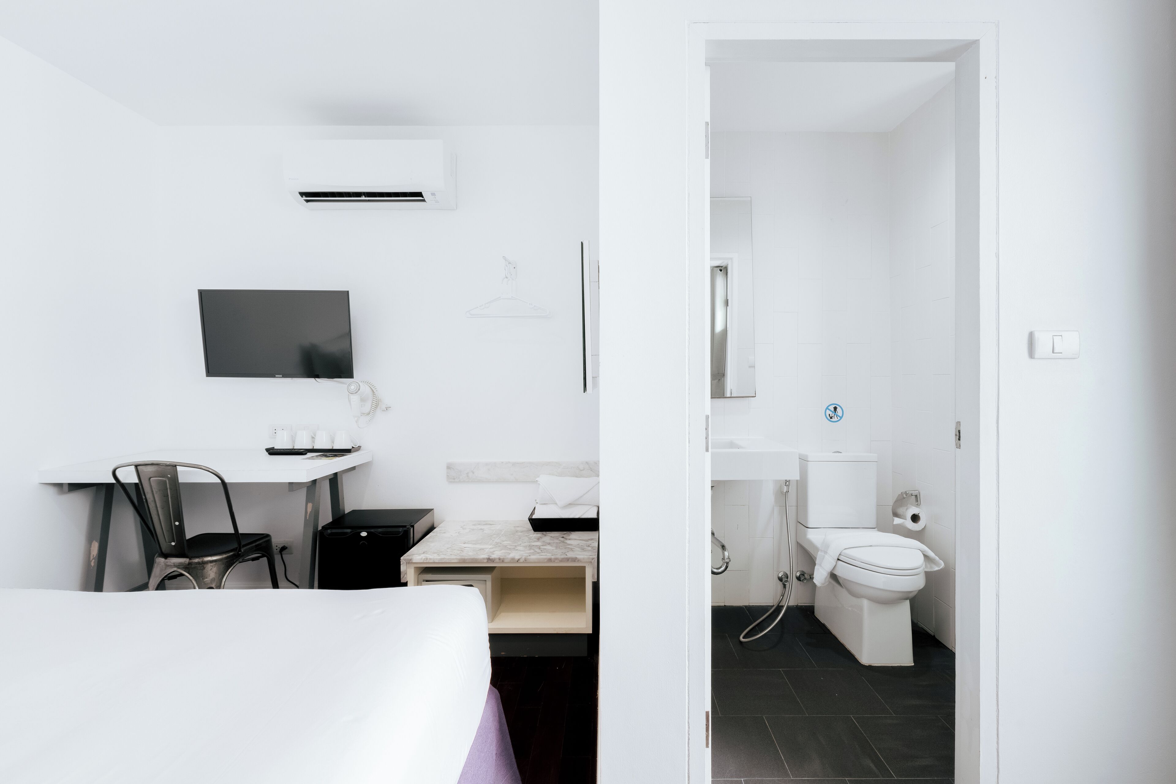 A hotel room with a bed, a desk with a chair, a television, a small table with cups, and a bathroom with a toilet and sink.