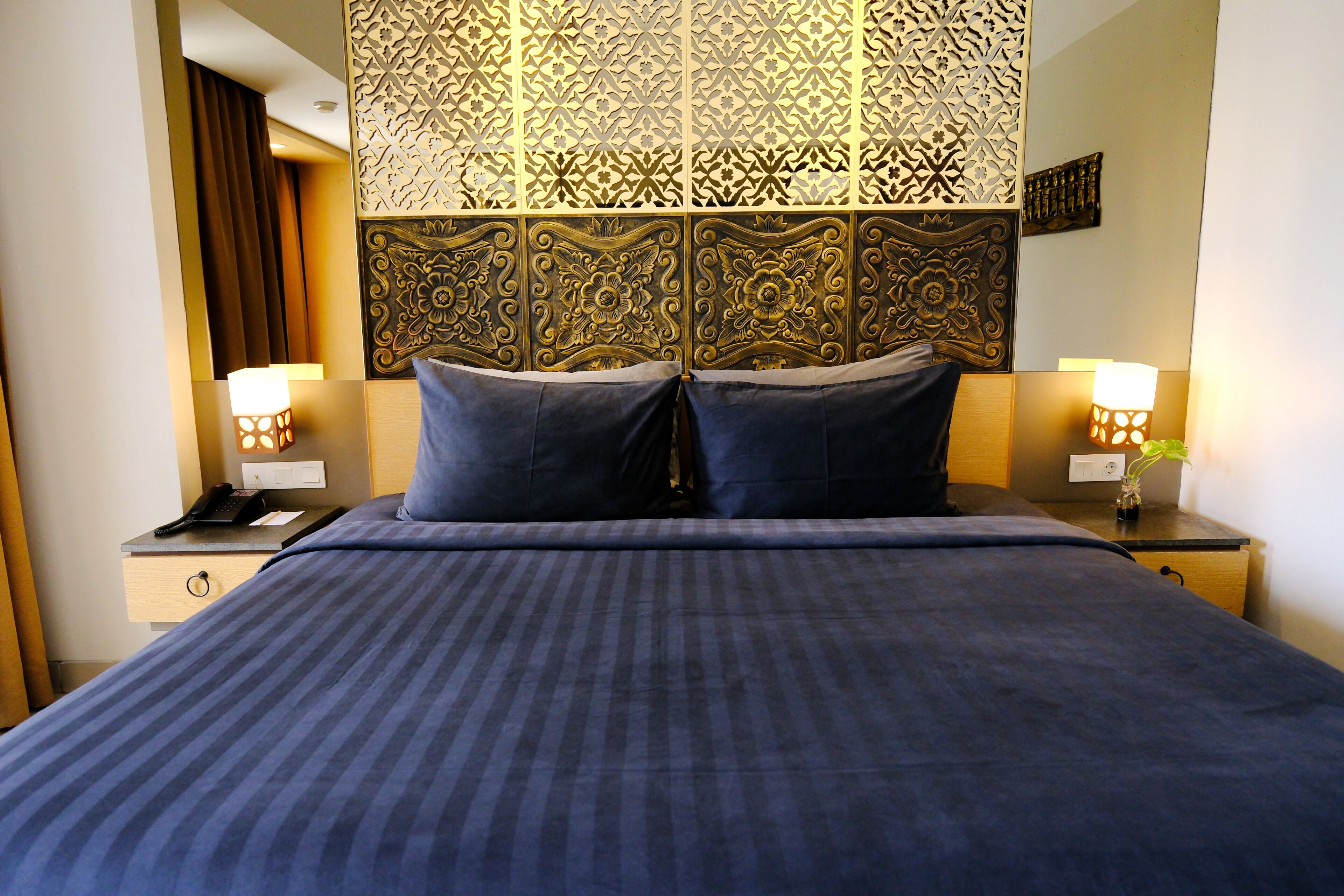 Una habitación de hotel con una cama grande, dos mesitas de noche, un cabecero decorativo y lámparas fijadas a la pared.