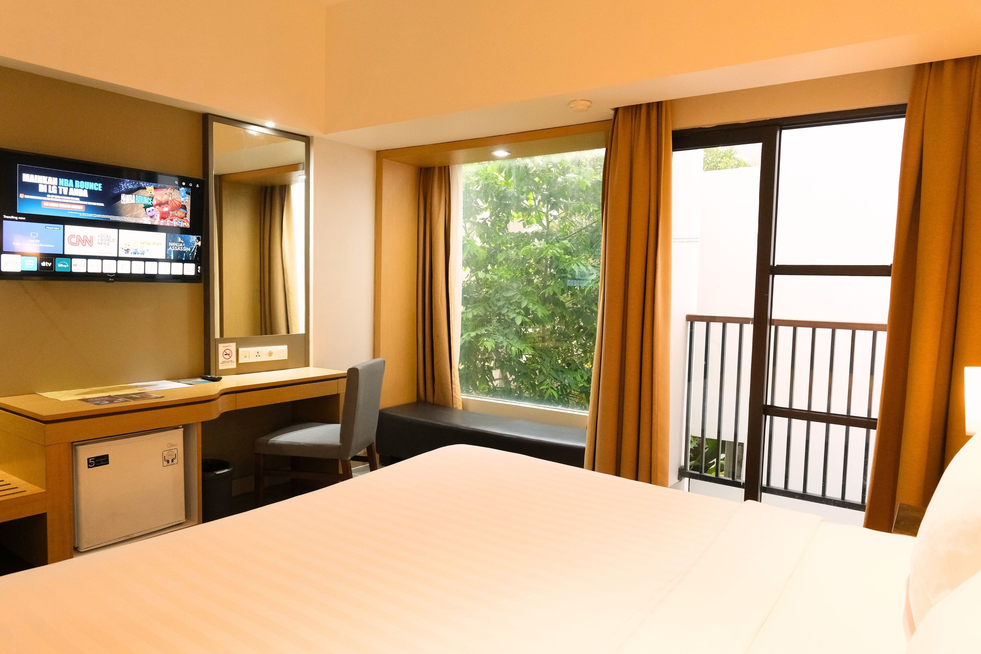 A hotel room with a bed, a desk, a chair, a television, and a window with curtains.