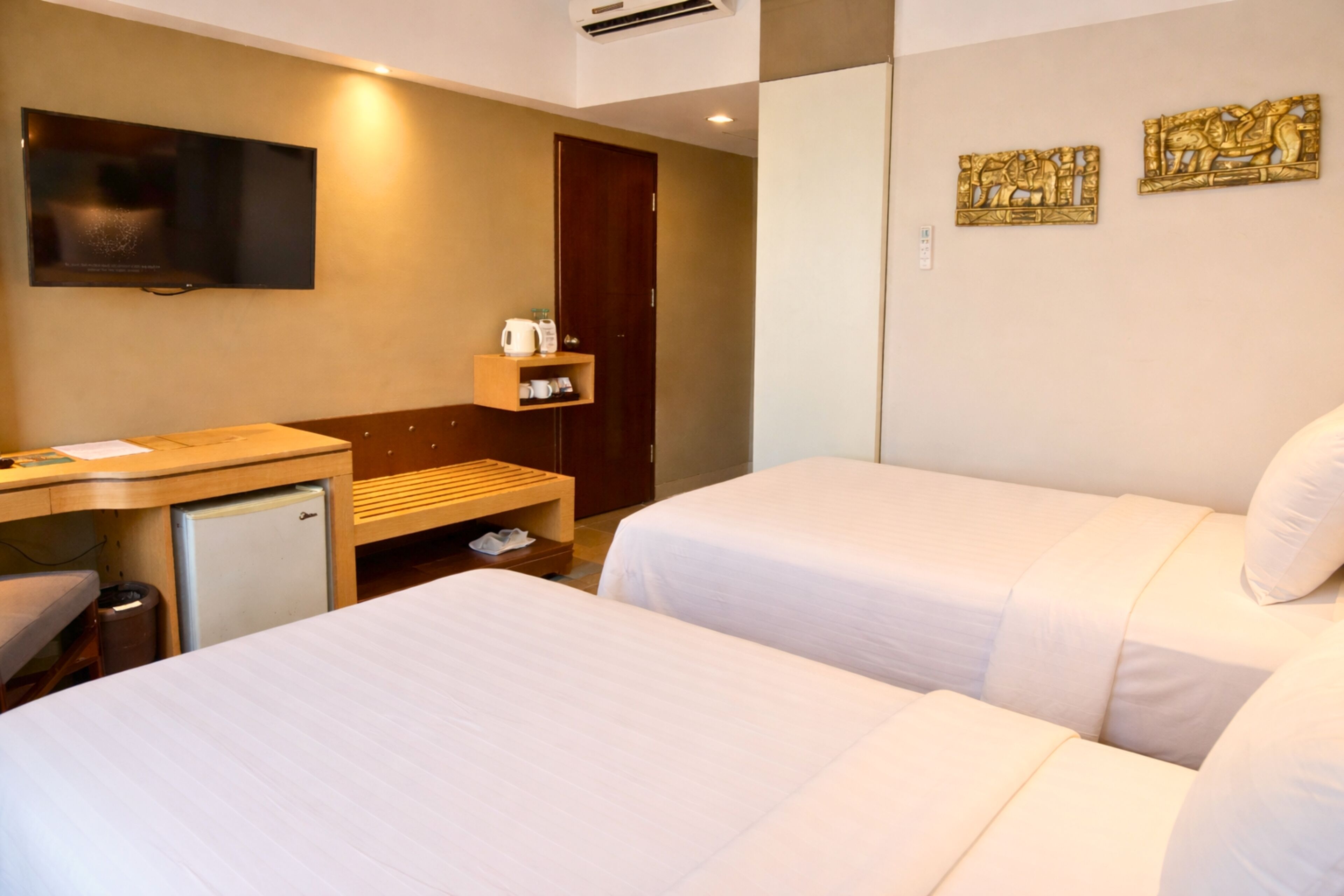 A hotel room with two beds, a desk with a computer, a small fridge, a TV, and a door.