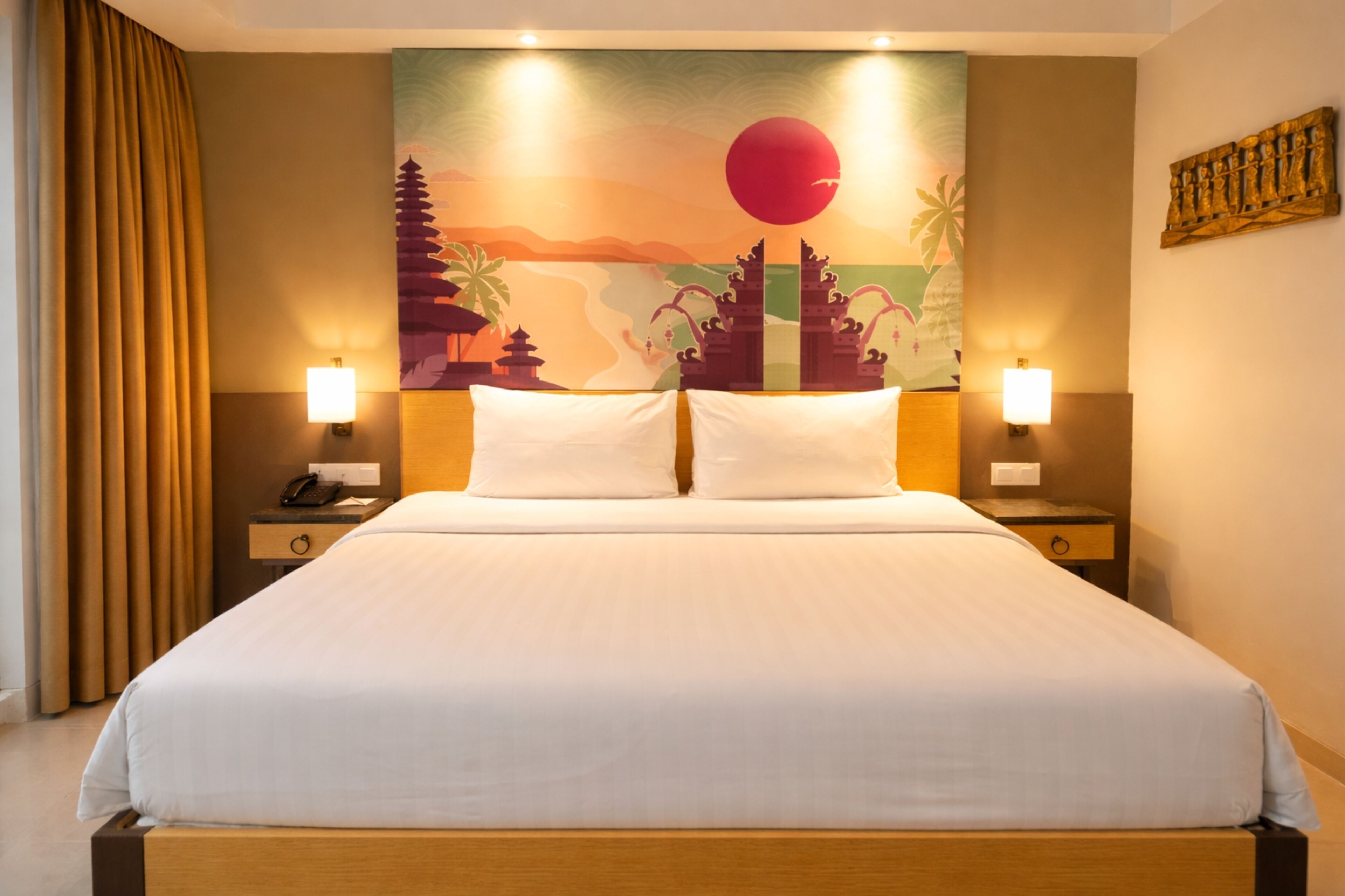 A hotel room with a bed, two bedside lamps, a nightstand with a phone, and a wall mural.