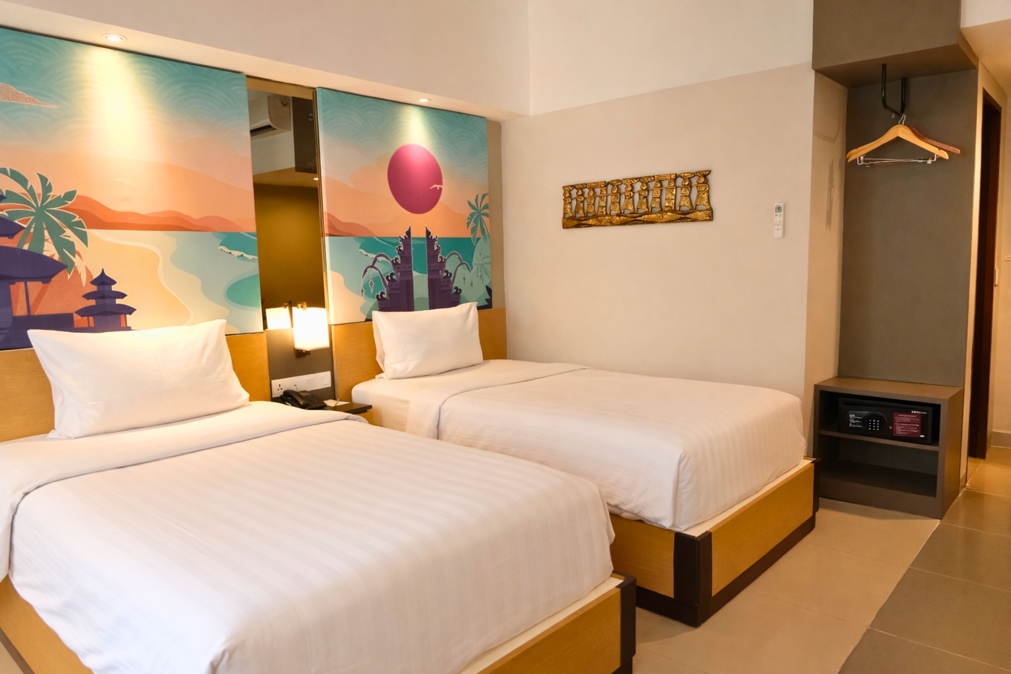 A hotel room with two beds, a nightstand, a wall art depicting a sunset, a coat rack, and a small shelf with a device.