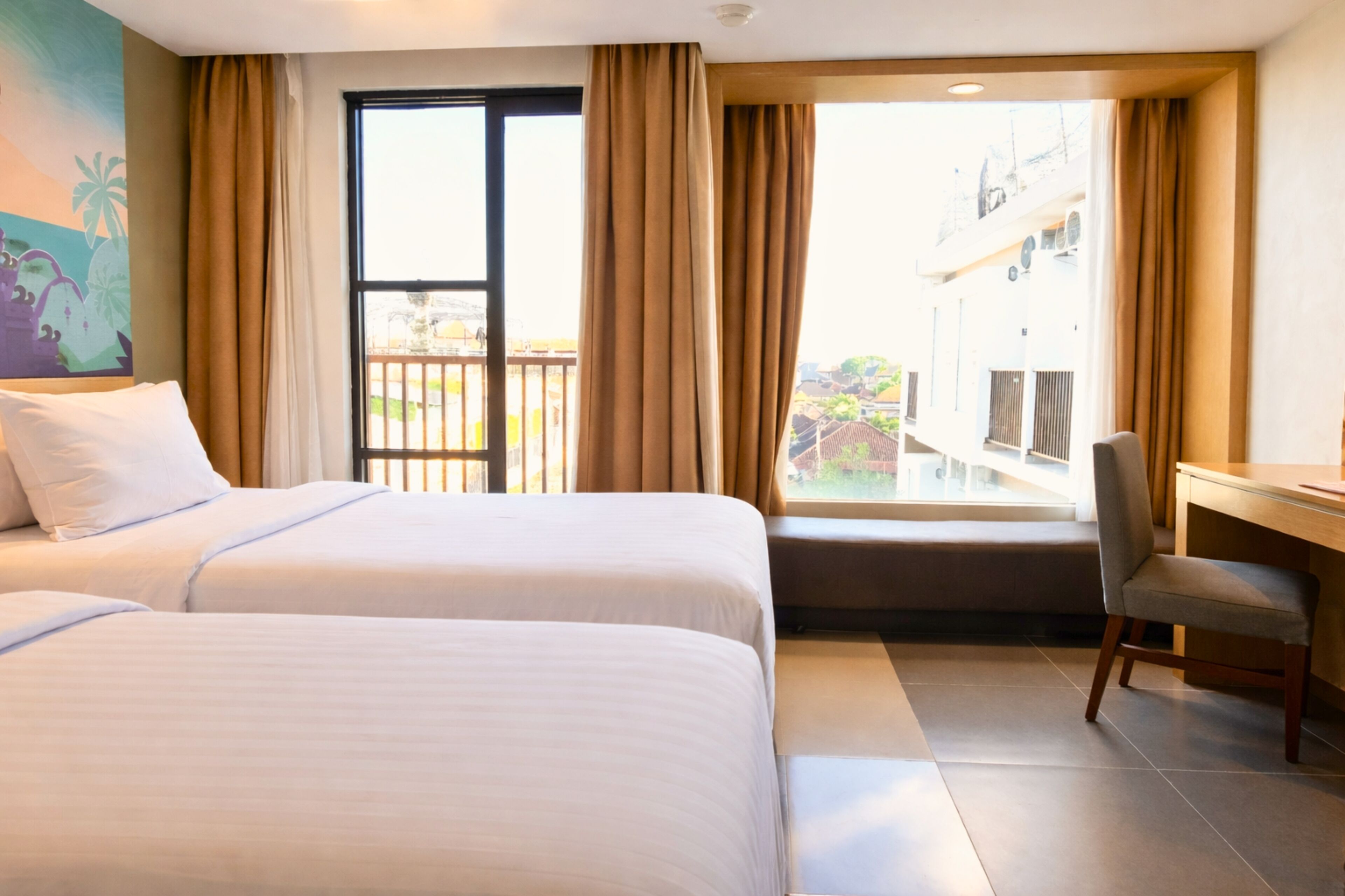 A hotel room with two beds, a desk, a chair, a balcony with a view, and a painting on the wall.