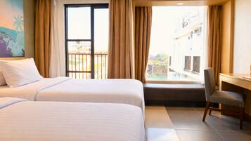 A hotel room with two beds, a desk, a chair, a balcony with a view, and a painting on the wall.