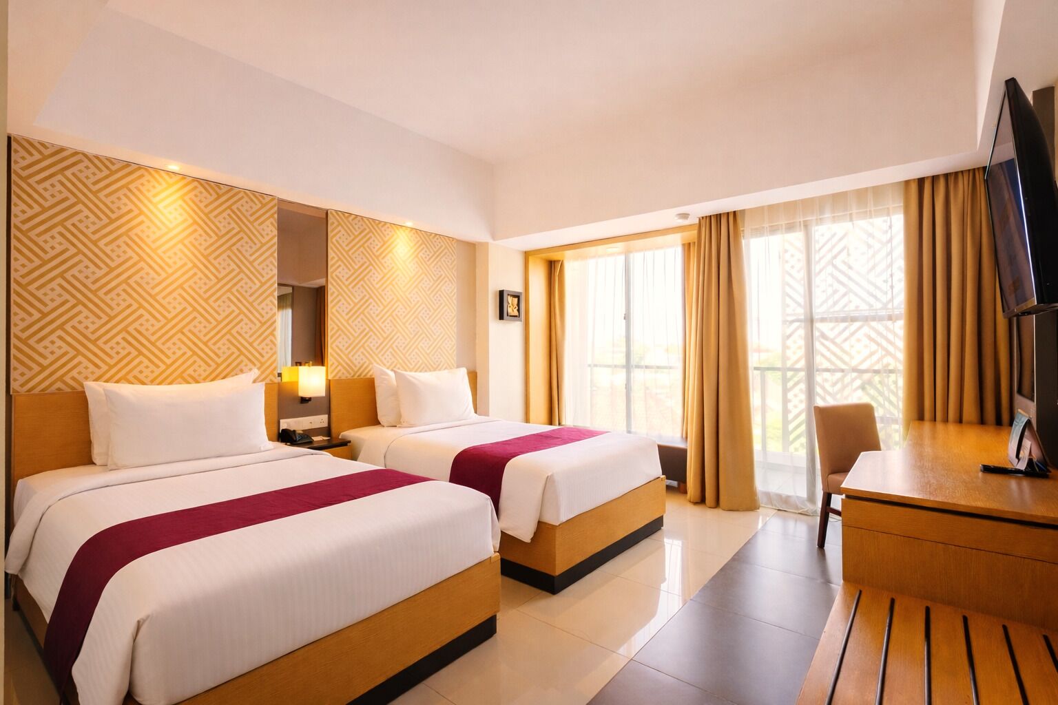 A hotel room with two beds, a desk, and a television.