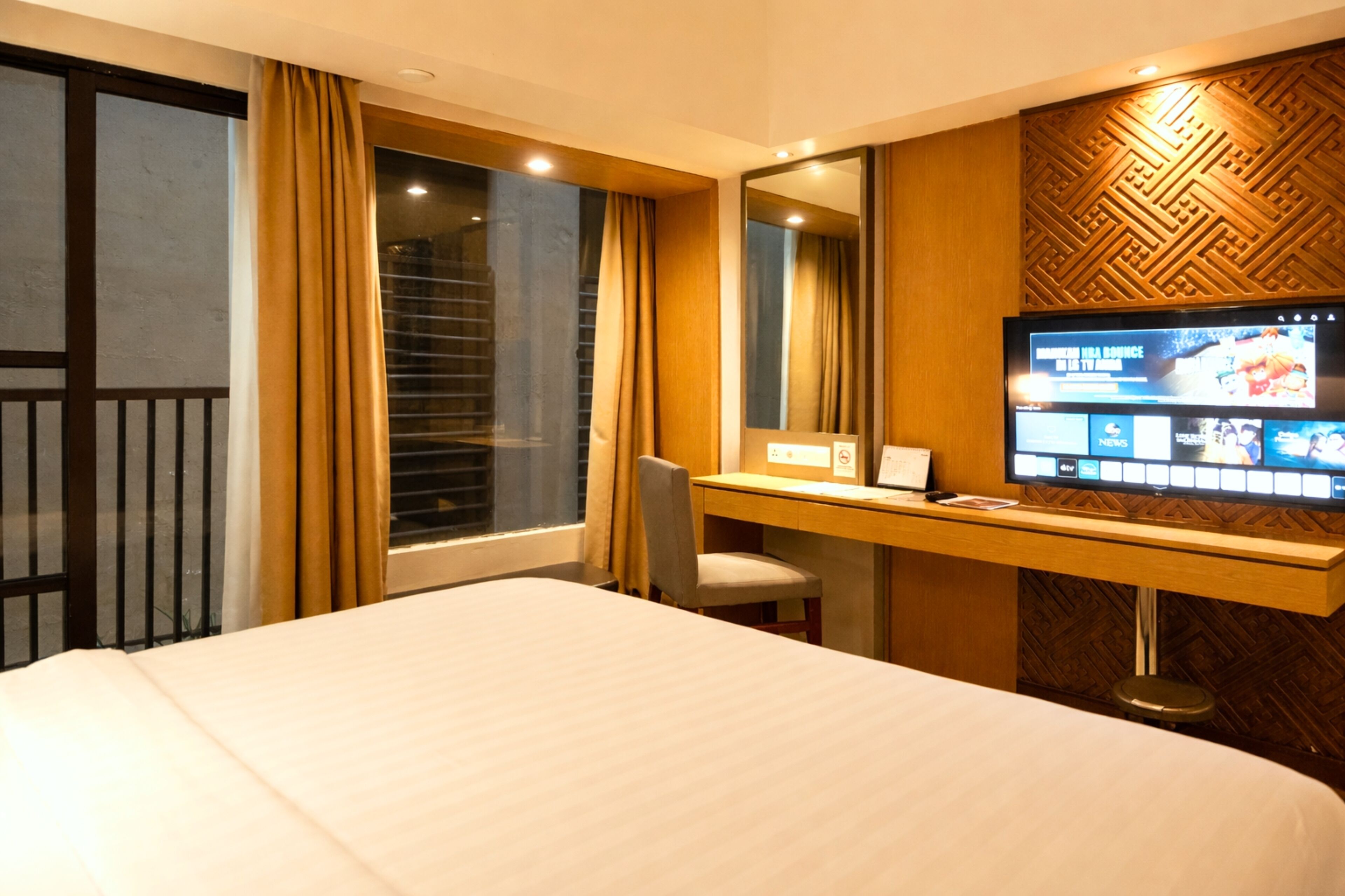 A hotel room with a bed, a desk with a computer, a TV, and a window with curtains.
