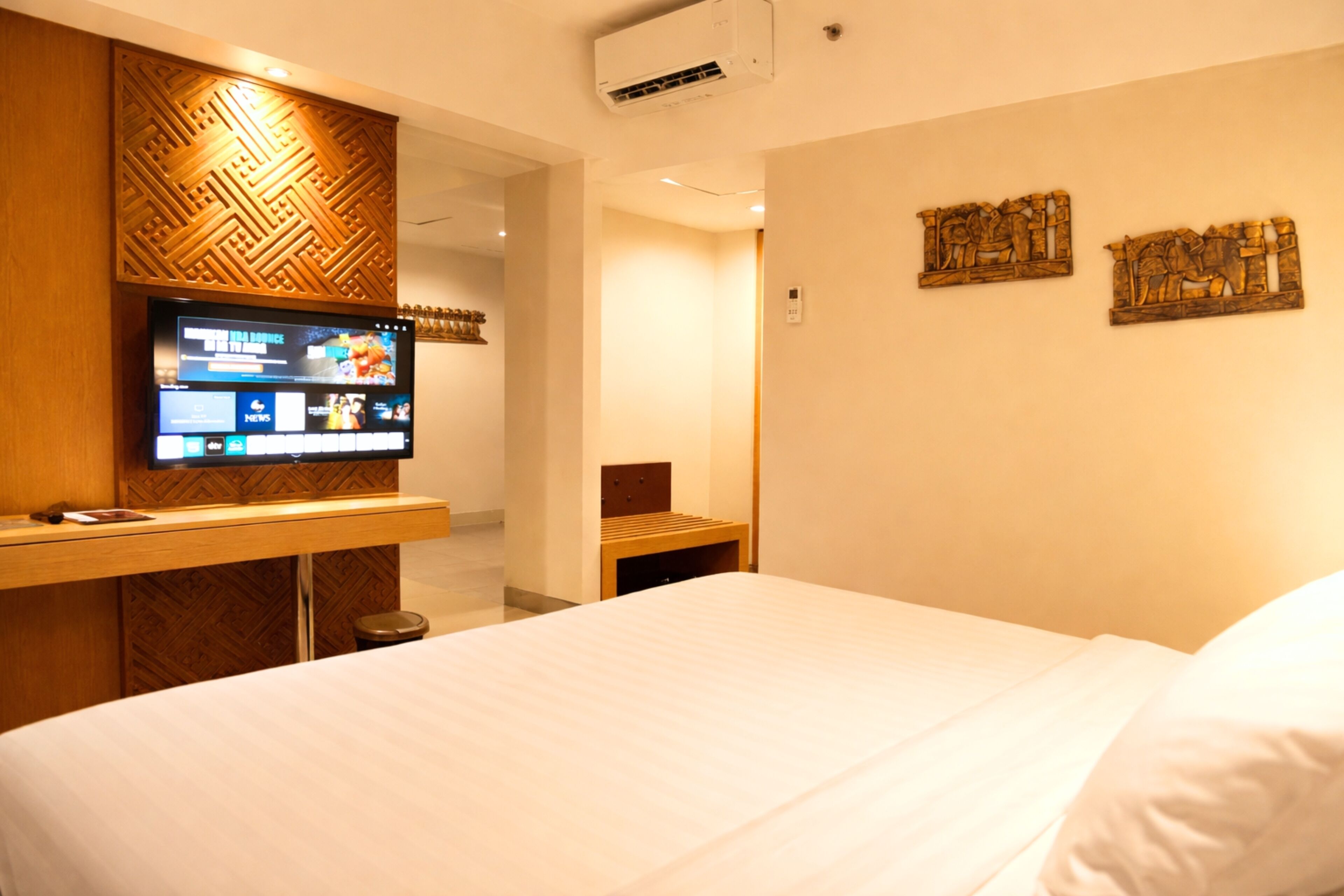 A hotel room with a bed, a TV mounted on a wooden panel, and two wall art pieces.