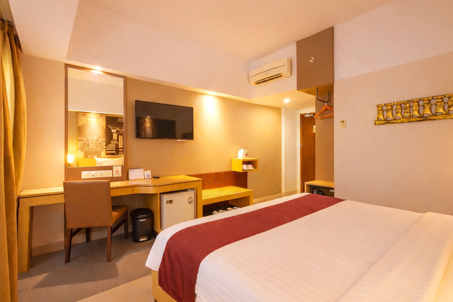 A hotel room with a bed, desk, chair, TV, and a small refrigerator.