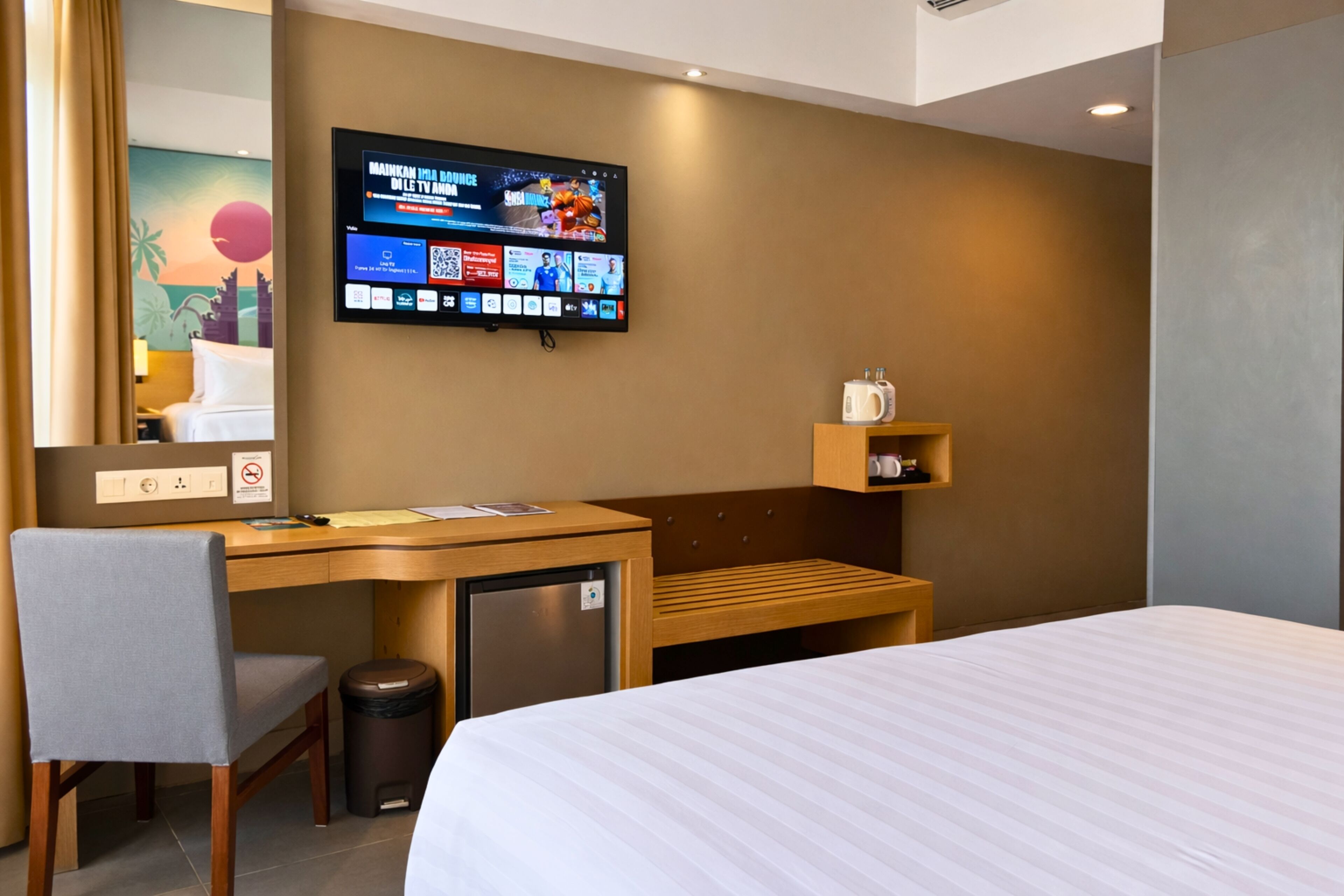 A hotel room with a bed, desk, chair, TV, and a small kitchenette area.