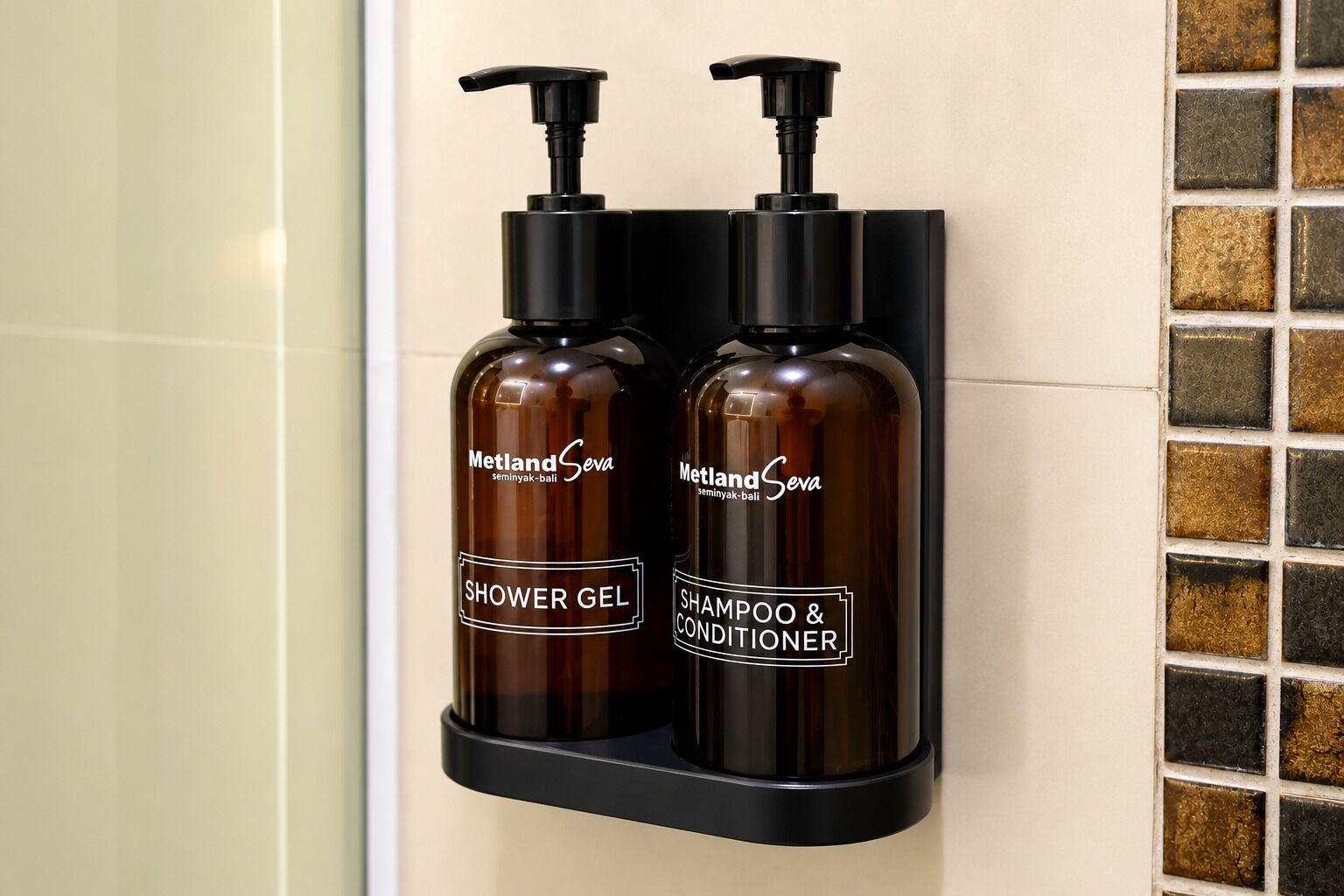 Deux flacons de la marque Metland Sewa sont fixés sur un mur noir, l’un portant l’étiquette « gel douche » et l’autre « shampoing et après-shampoing ».