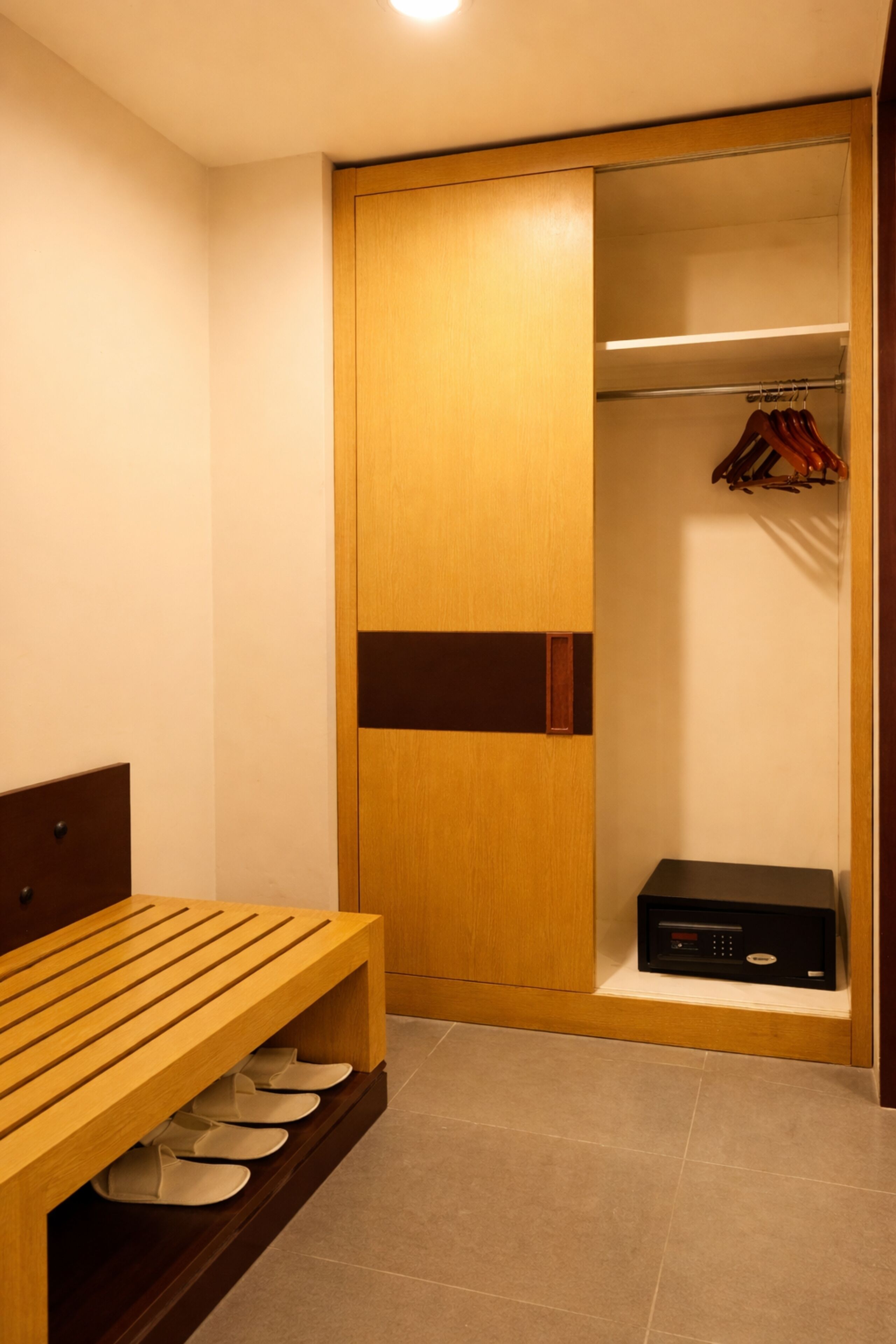 A walk-in closet with a wooden bench and shoe storage, a hanging rack, and a small electronic device on a shelf.