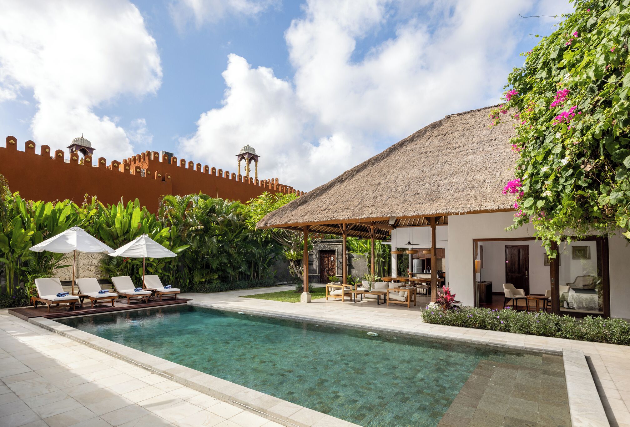 A pool area with lounge chairs, a thatched-roof structure, and a view of a historic wall with towers.