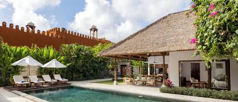 A pool area with lounge chairs, a thatched-roof structure, and a view of a historic wall with towers.