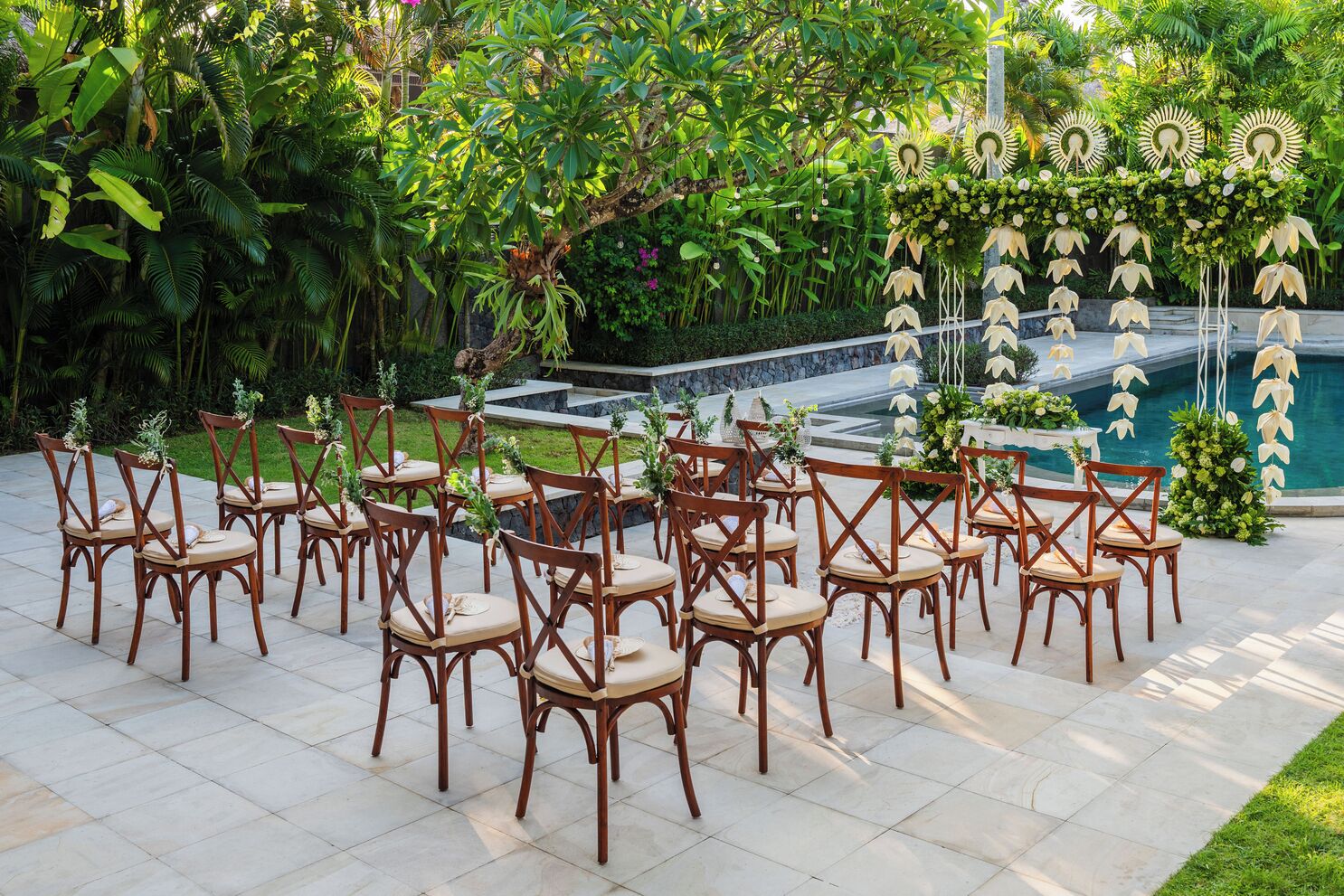 Un espace extérieur aménagé avec des chaises et des tables en bois, entouré d’une végétation luxuriante et agrémenté d’une composition décorative de fleurs et de feuilles.