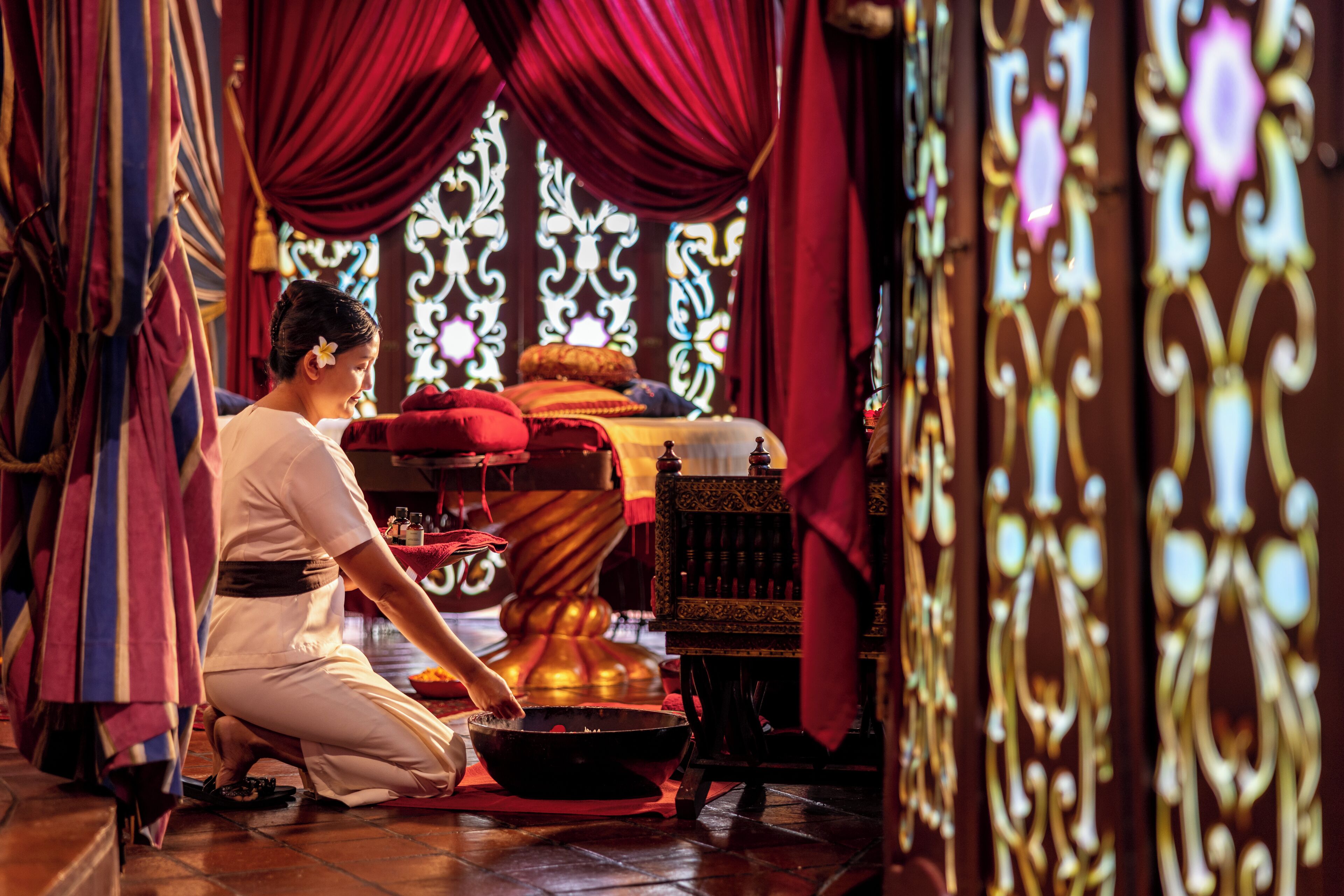 A person kneeling in a room with a traditional chair and a table with a bowl.