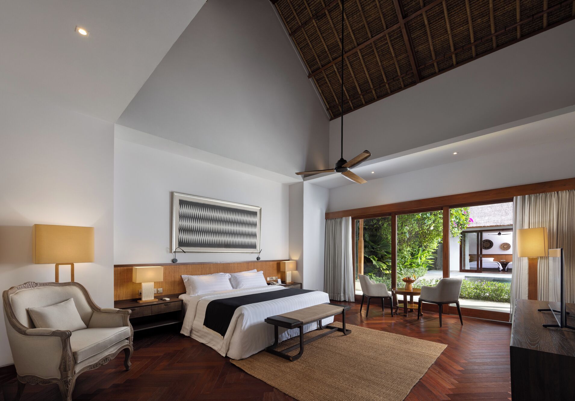A spacious bedroom with a large bed, a ceiling fan, a view of greenery outside, and a modern design.