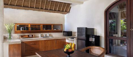 Una cocina con armarios de madera, un microondas y un refrigerador. Hay un frutero sobre la mesa y una silla.