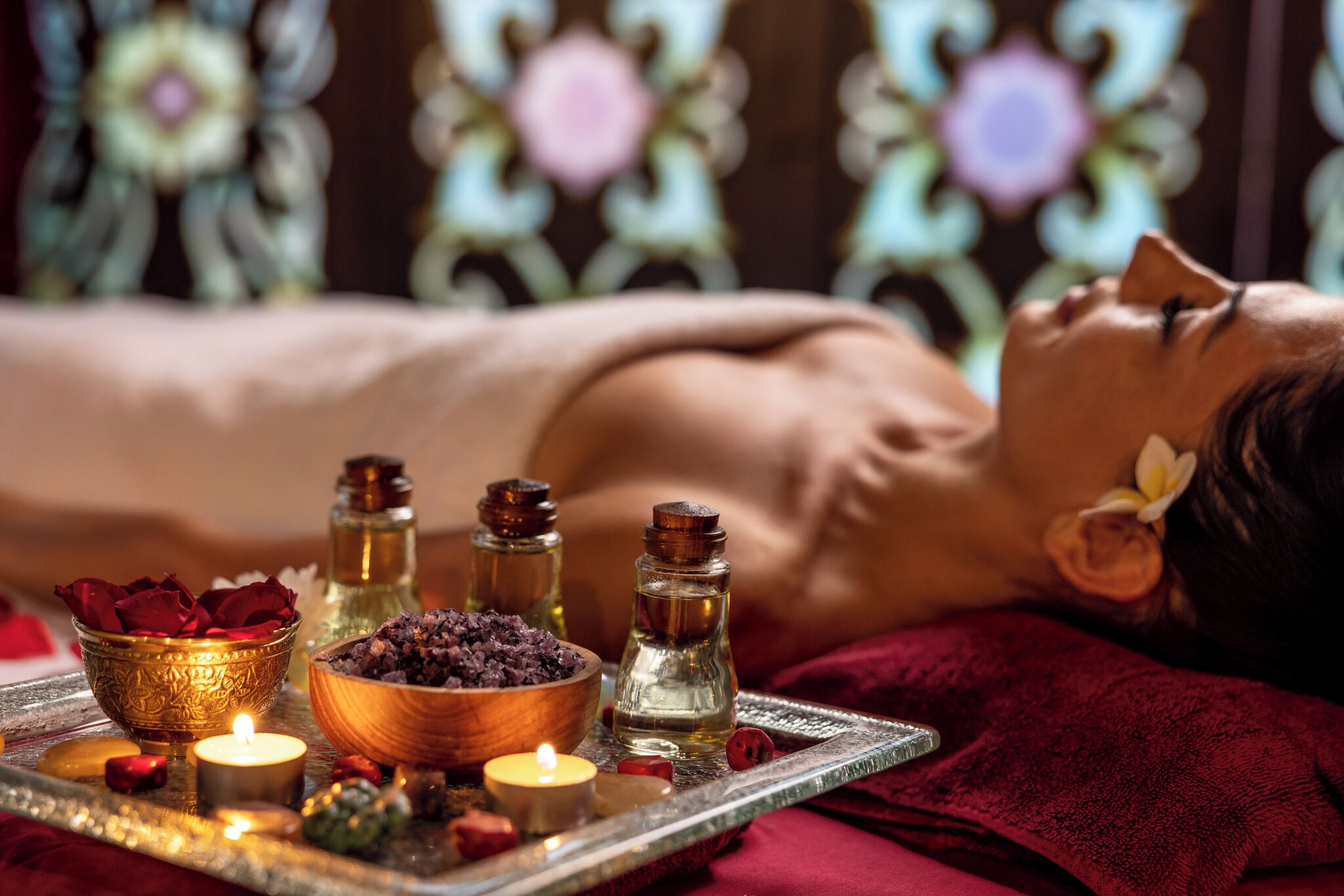 Iemand ontvangt een massage, met een dienblad vol kaarsen, essentiële oliën en rozenblaadjes.