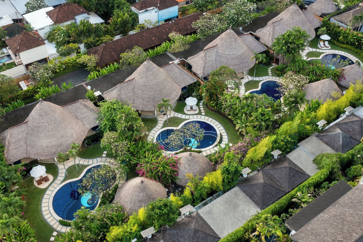 An aerial view of a resort with multiple thatched-roof structures, swimming pools, and lush greenery.