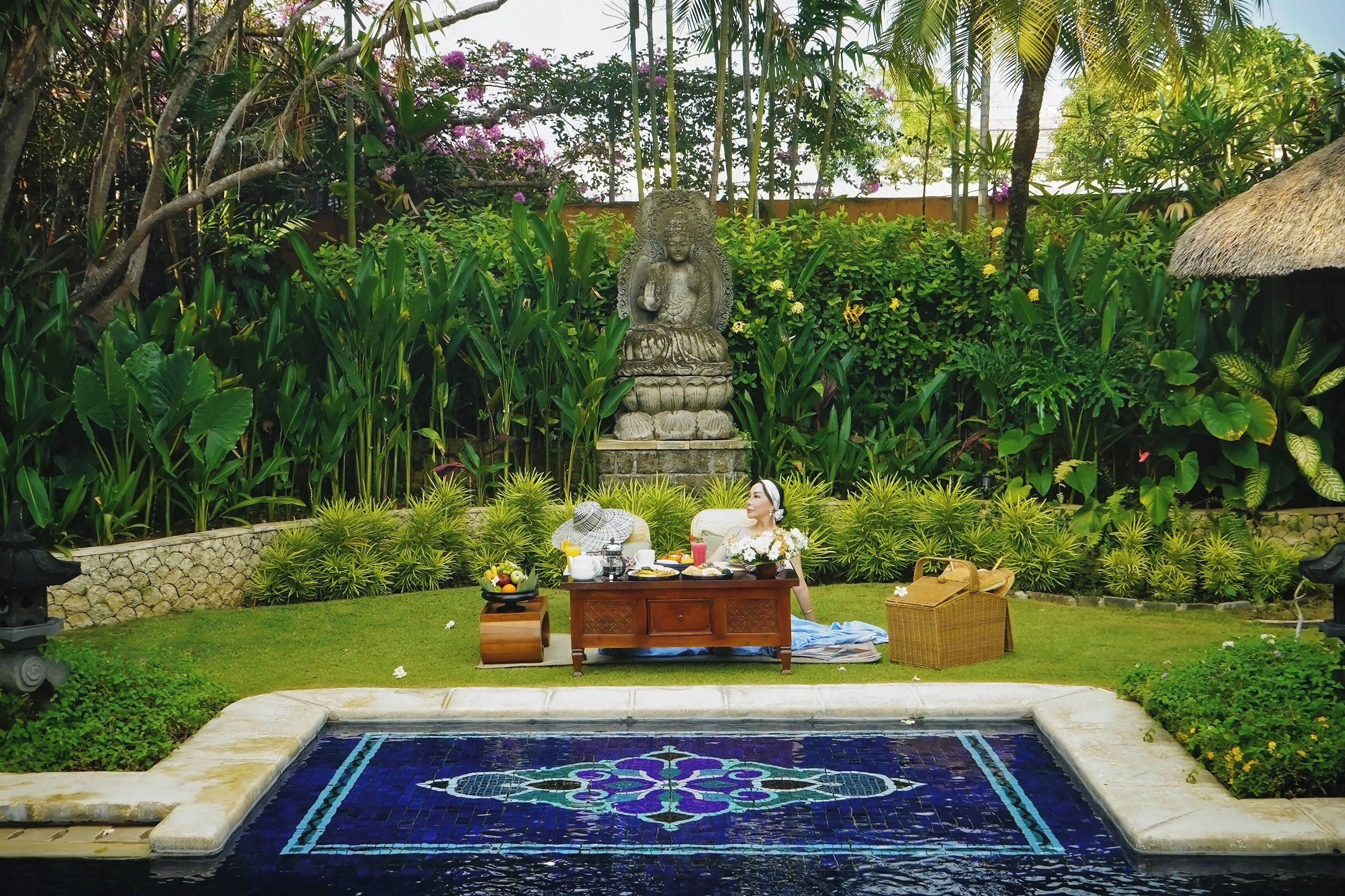 Un jardín tranquilo con una estatua, un comedor y una piscina decorativa.