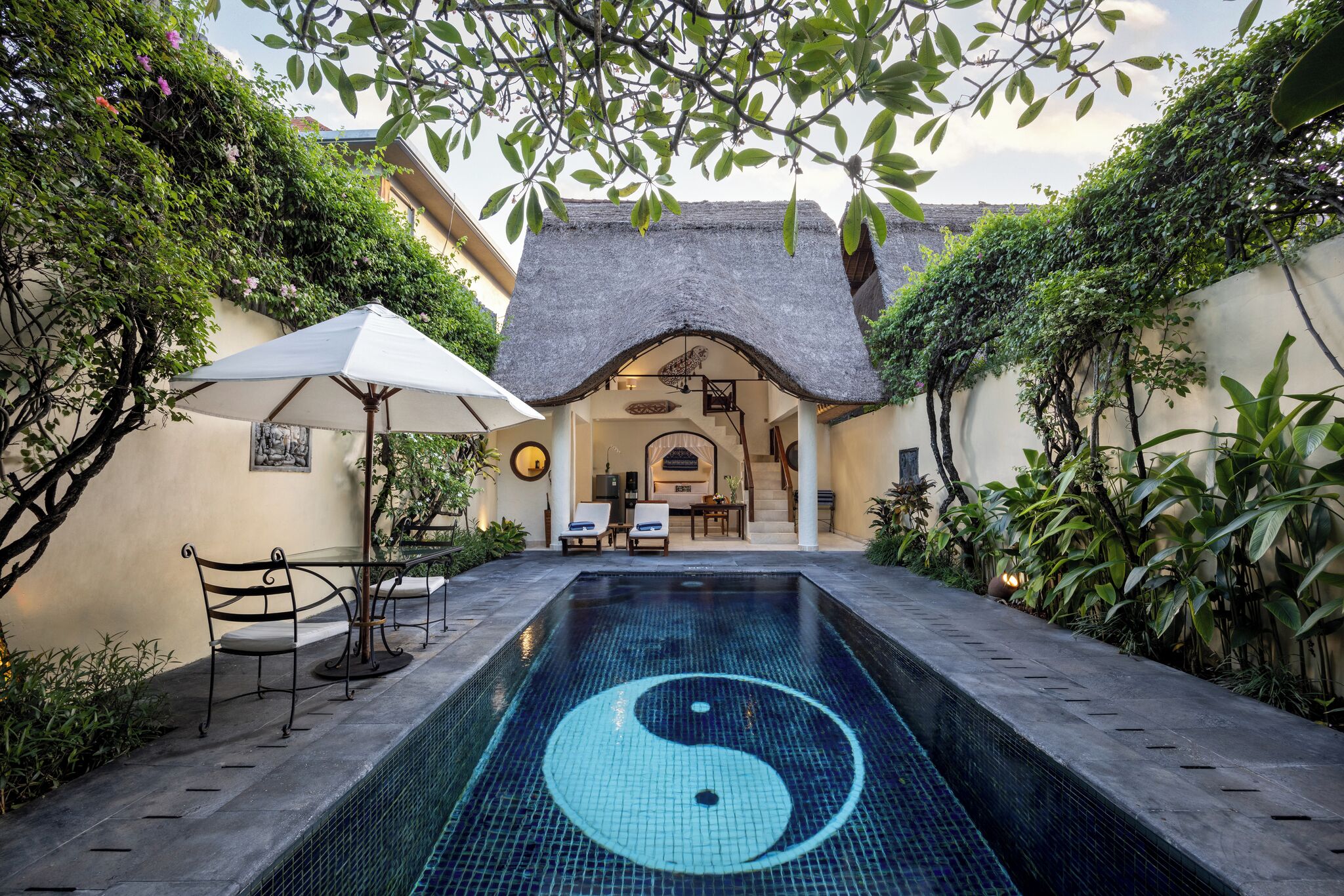 Una piscina con un símbolo yin-yang, rodeada por un patio con sillas y un paraguas.