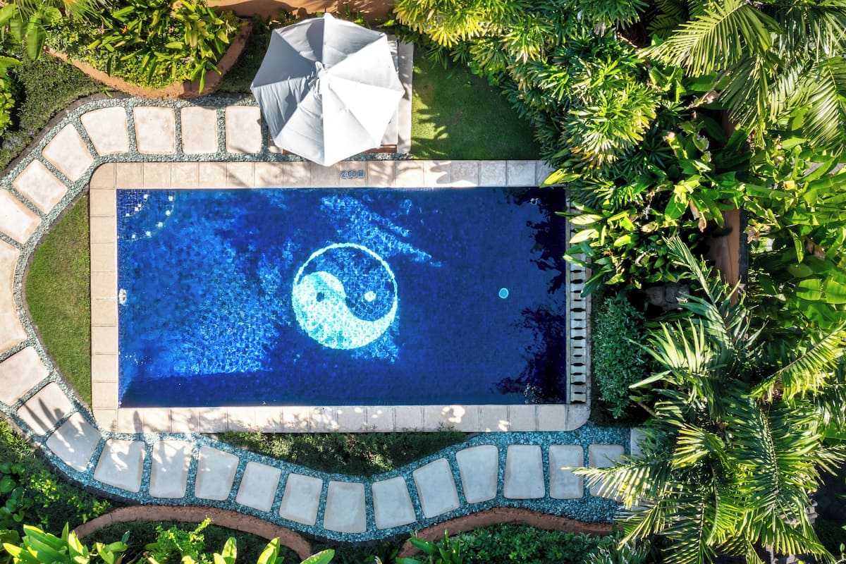 An aerial view of a rectangular pool with a yin-yang symbol in the center, surrounded by a stone pathway and lush greenery.