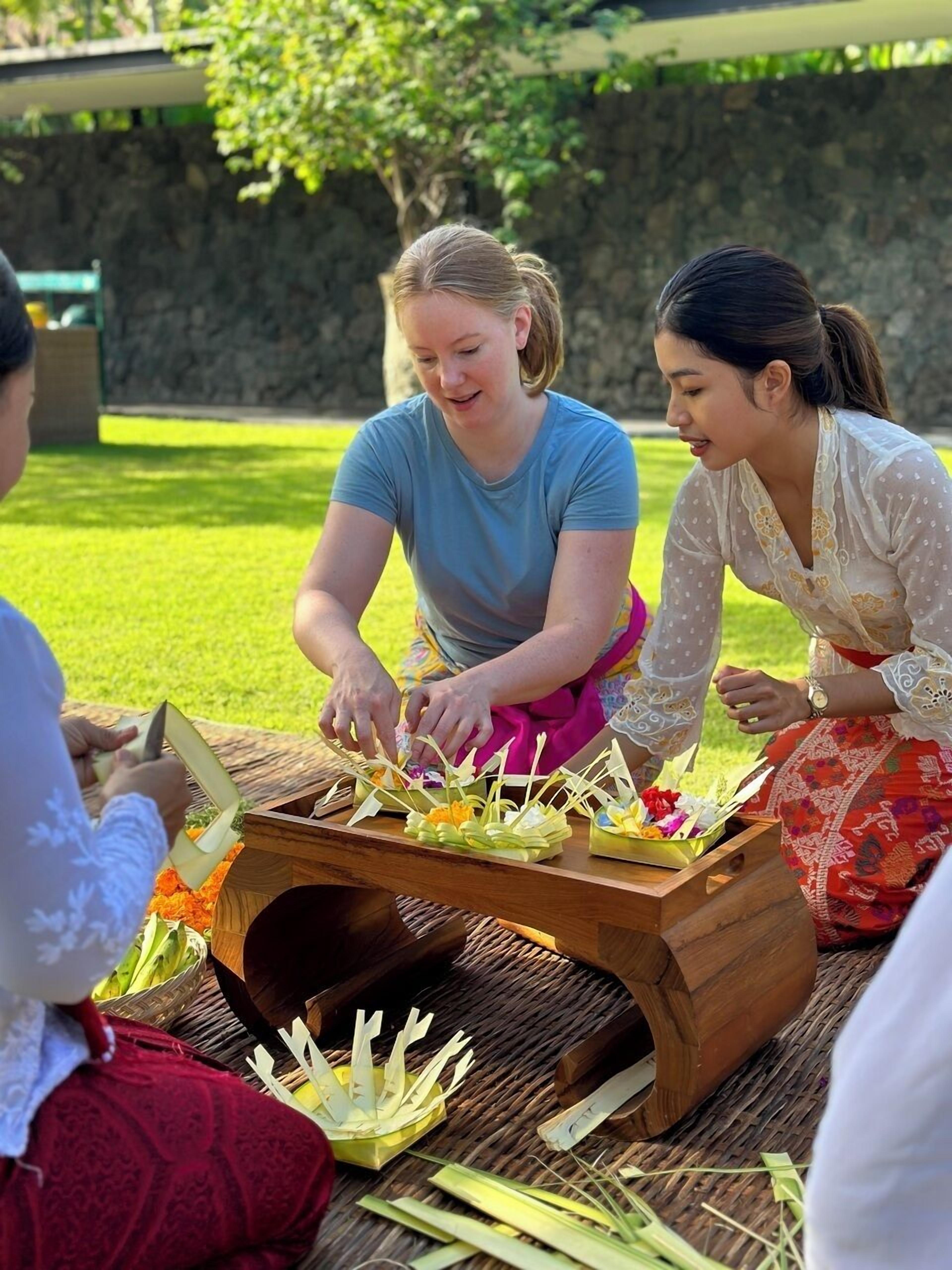 Three individuals engaged in an outdoor activity with a wooden structure, possibly a traditional or cultural setup, surrounded by greenery.