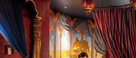 A room with a decorative ceiling, a bed with a patterned bedspread, and a small table with candles.