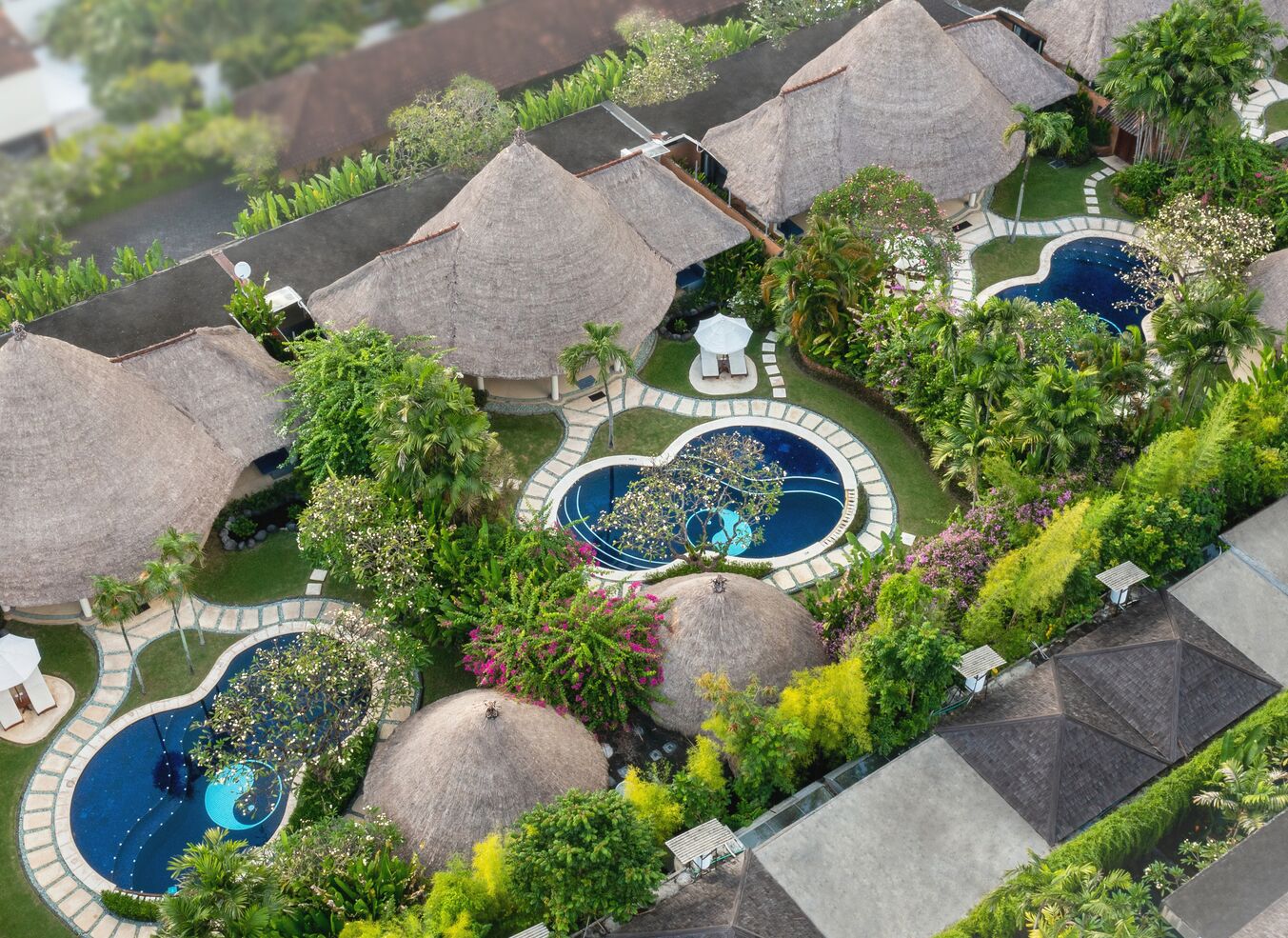 A resort with multiple thatched-roof structures, swimming pools, and lush greenery.