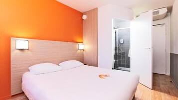 Una camera d'albergo con un letto, un armadio bianco e un angolo doccia.
