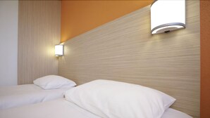 Habitación de hotel con dos camas, cada una con ropa blanca y almohadas. Hay una lámpara de pared sobre las camas.