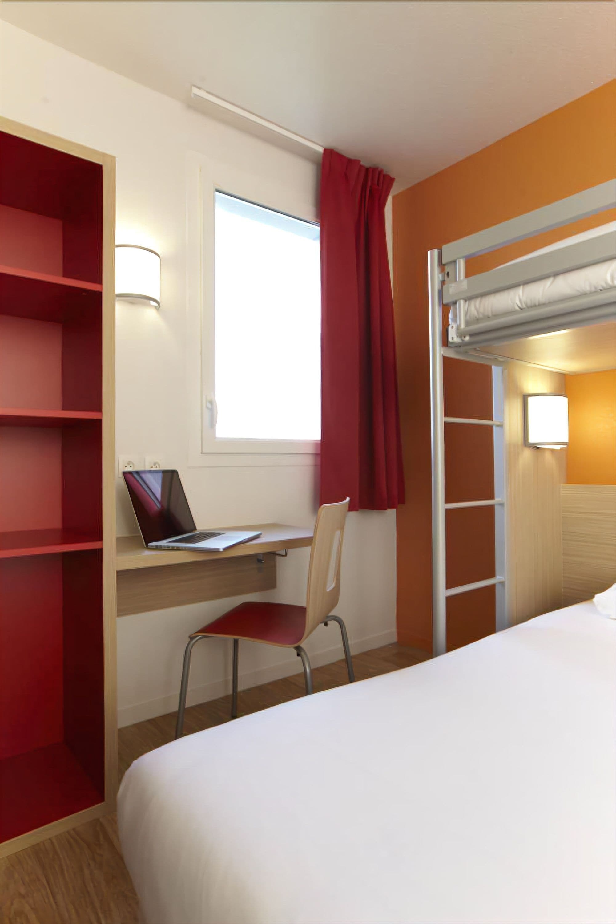 Hotelkamer met een bed, een bureau met een laptop, een stoel, een trap en een raam met gordijnen.