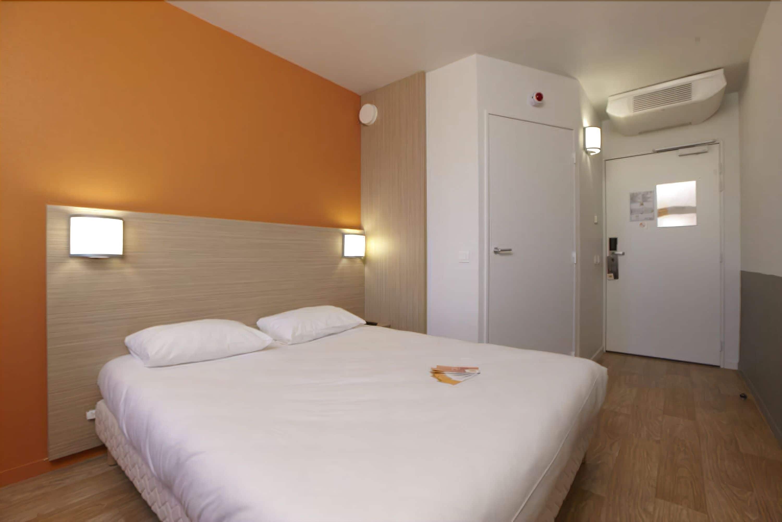 A hotel room with a bed, a door, and a wall-mounted air conditioner.