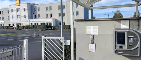 Entrada de hotel con zona de estacionamiento protegida, una caseta de seguridad y cielo despejado.