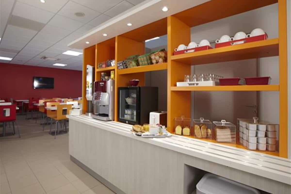 A cafeteria with a counter, shelves with dishes, and a refrigerator.