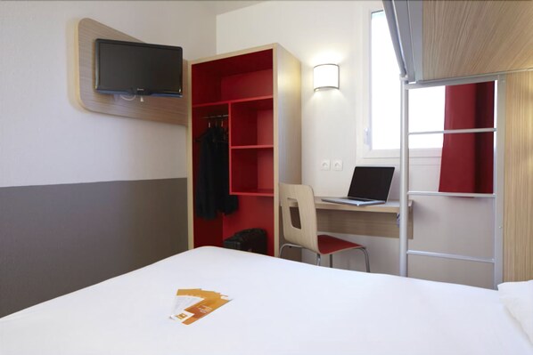 A hotel room with a bed, a desk with a laptop, a chair, a TV mounted on the wall, and a wardrobe with red shelves. - Hôtel Première Classe Caen Nord - Mémorial (Saint-Contest)