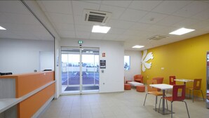Un interior moderno con mostrador de recepción, zona de estar y una pared de acento amarilla.
