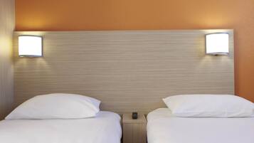 A hotel room with two single beds, each with a white pillow and a nightstand with a remote control.