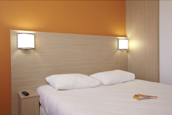A neatly made bed with white linens and two pillows, a bedside table with a remote control, and two wall-mounted light fixtures. - Hôtel Première Classe Caen Nord - Mémorial (Saint-Contest)