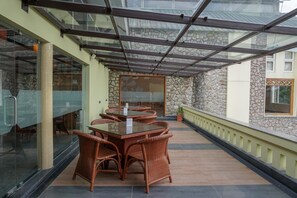 Un espace extérieur abrité, aménagé pour les repas, avec des meubles en osier et une table en verre.
