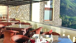 Een restaurant met rieten meubels, stenen muren en een glazen dak met uitzicht op een schilderachtig landschap.