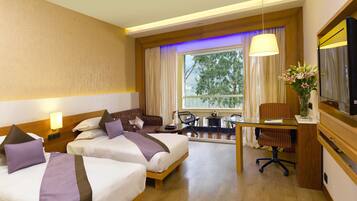 A hotel room with two beds, a desk, a chair, a TV, and a window with curtains.