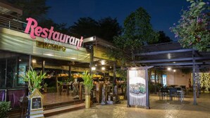 A restaurant with a covered outdoor seating area, a signboard, and potted plants. - Ploykhumthong Boutique Resort (Bangkok)