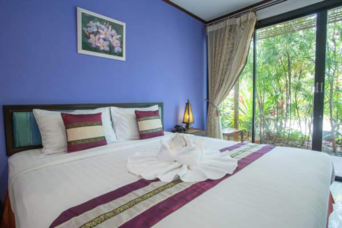Habitación de hotel con una cama grande, una mesita de noche, una lámpara y vistas a zonas verdes por la ventana.
