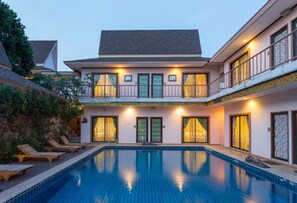 Um edifício de dois andares com piscina, varandas e fachada bem iluminada.