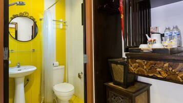 A bathroom with a yellow tiled wall, a white sink, a toilet, and a mirror. There is a wooden shelf with toiletries.