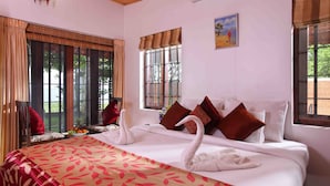 A hotel room with a large bed, two windows, a painting, and a fruit bowl on the nightstand. - Saro Lake County (Kottayam)