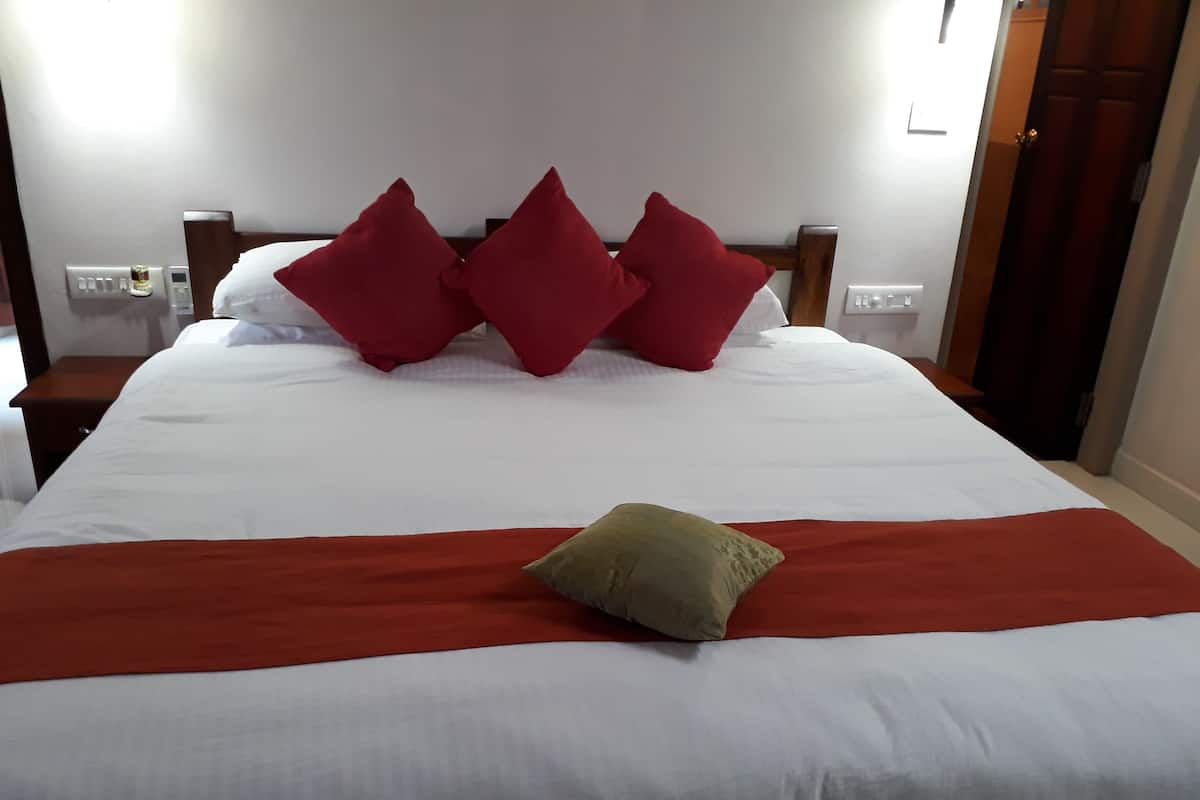 A neatly made bed with white bedding and a red blanket, accompanied by three red pillows and a single green pillow.
