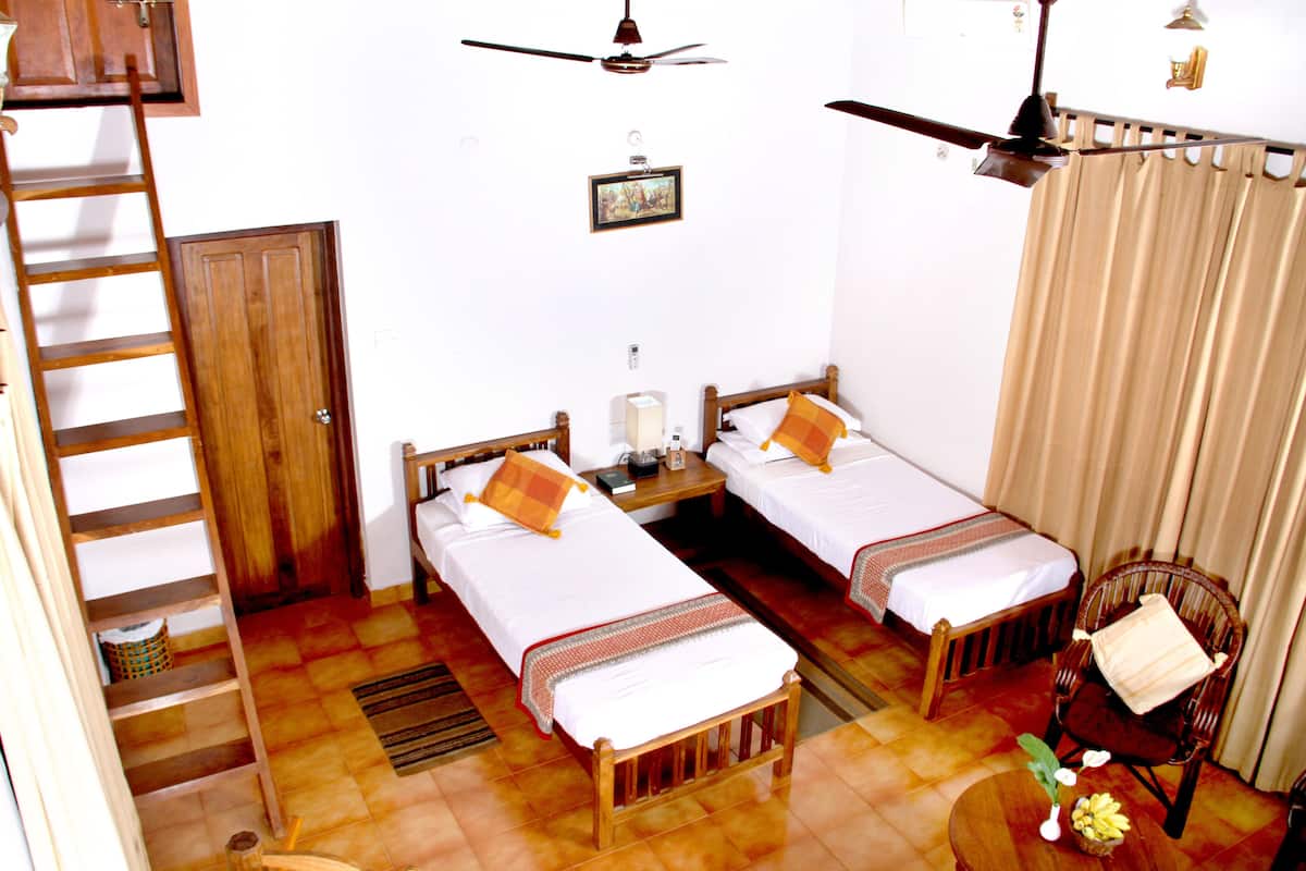 A hotel room with two single beds, a wooden chair, a small table with a vase, a ceiling fan, and a ladder leading to a door.