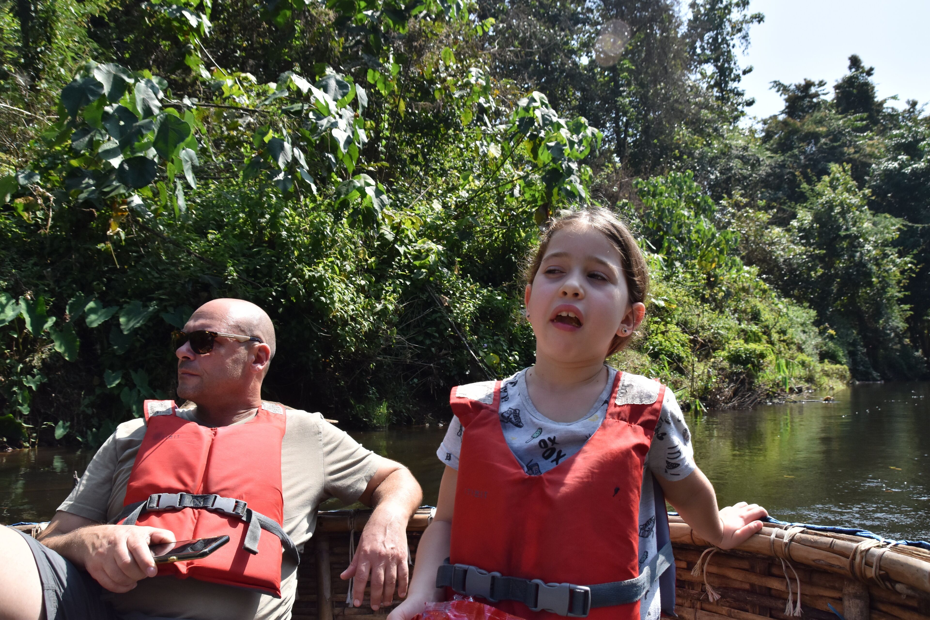 Two people in a boat with a river and dense greenery in the background.